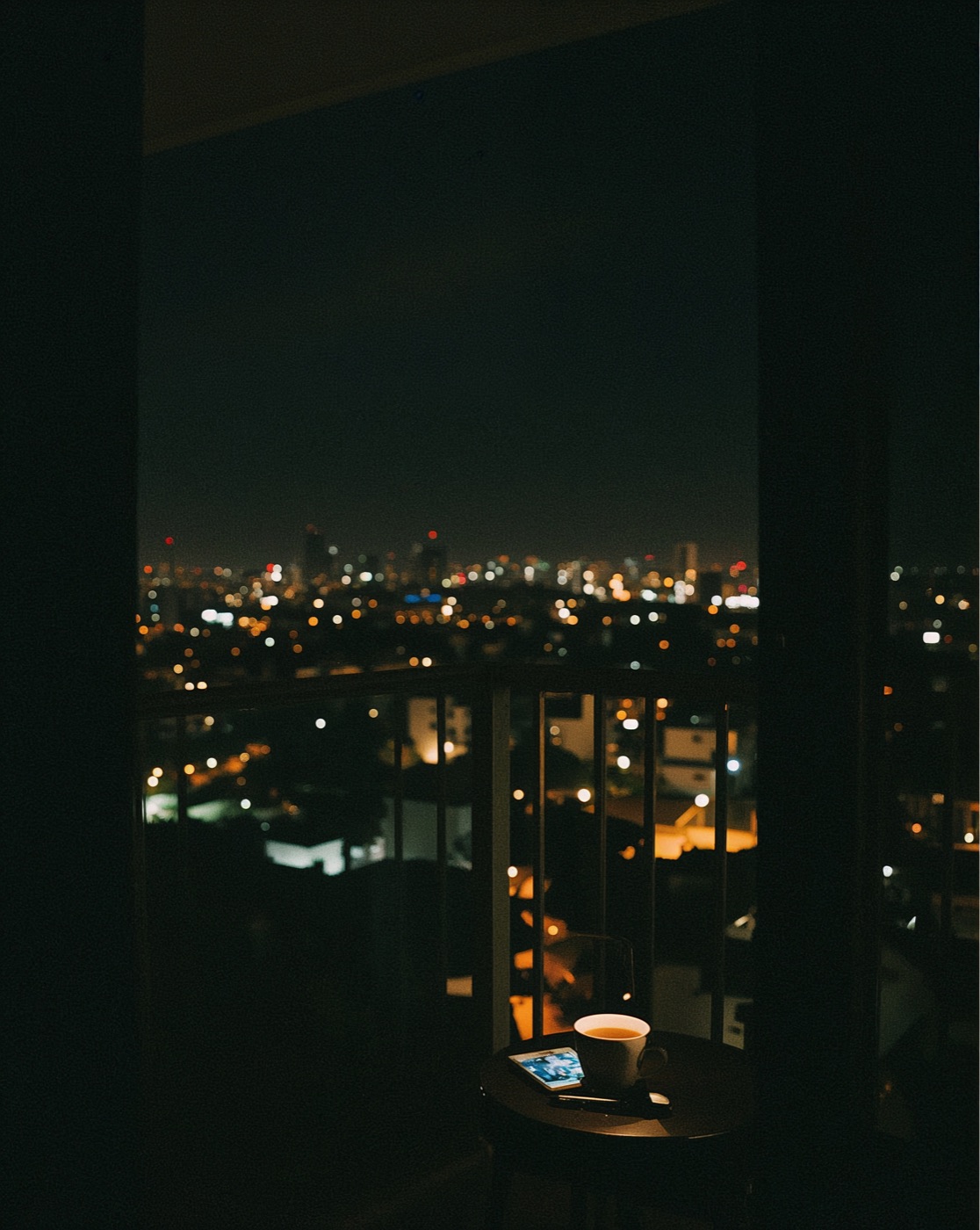 A cup of tea on a balcony table above the lights of a city at night